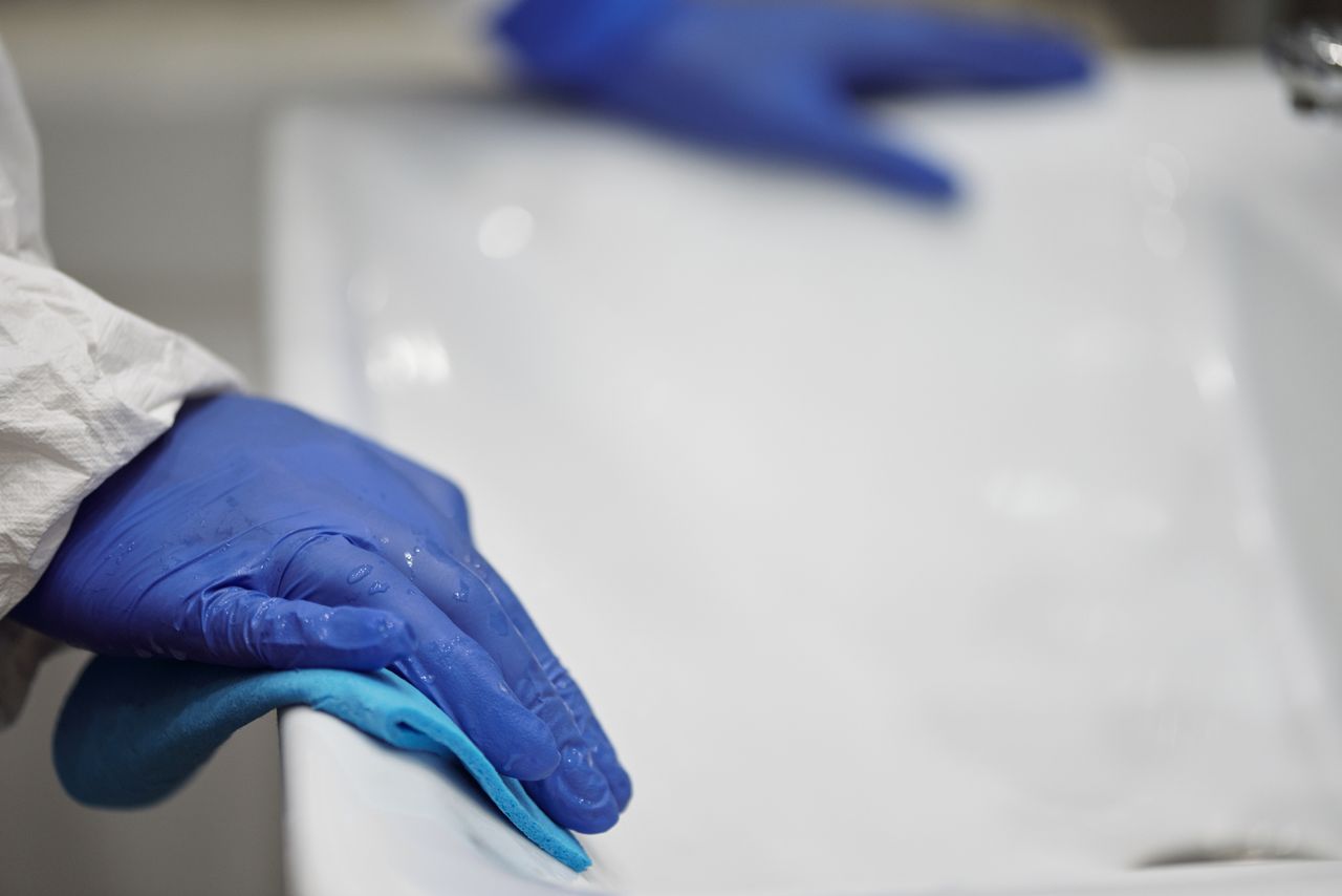 about-us Close-up of a person sanitizing a bathroom sink with gloves and cloth, focusing on hygiene and cleanliness.