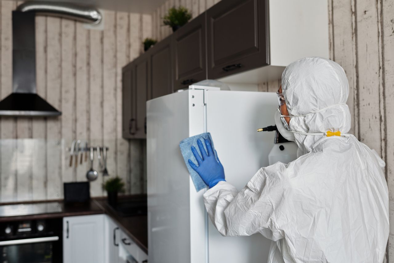 services-03 Individual in full protective gear cleaning kitchen fridge, promoting hygiene and safety.