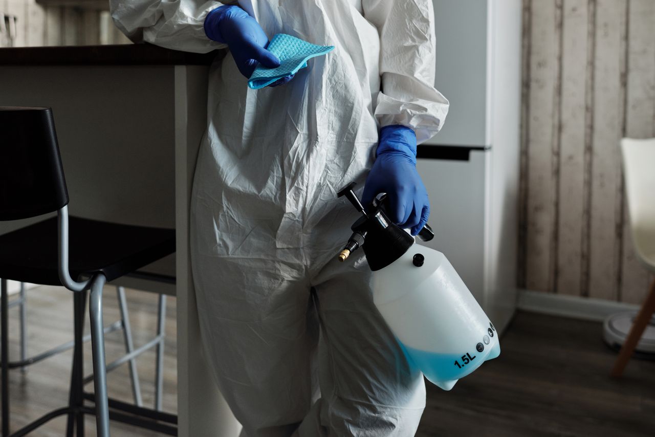 services-04 Individual in PPE holding a disinfectant spray bottle indoors for cleaning.